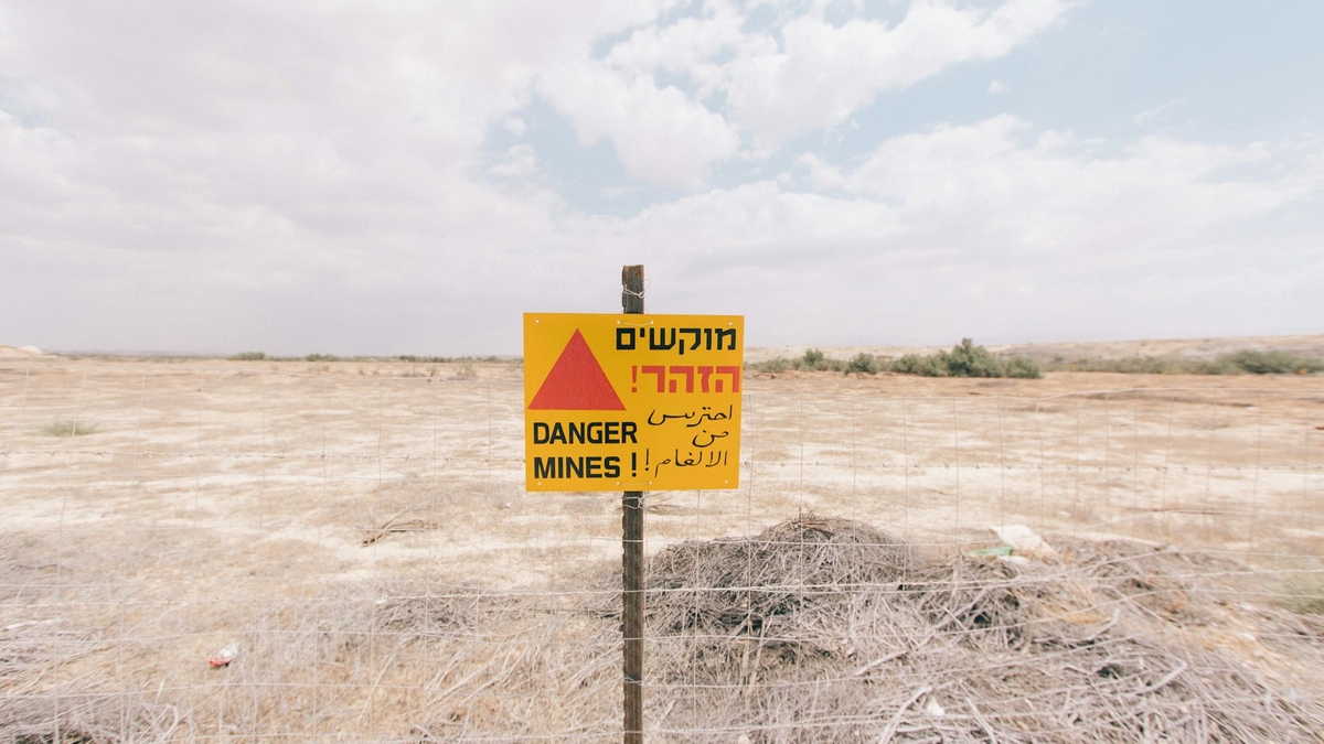 乾いた草地に立つ多言語の DANGER MINES 警告標識